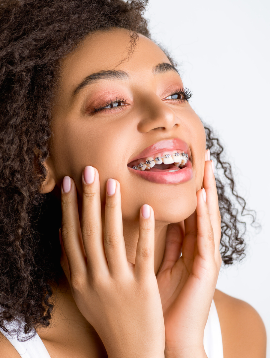 Beautiful, young black woman smiling with hands on her face showing off her braces.