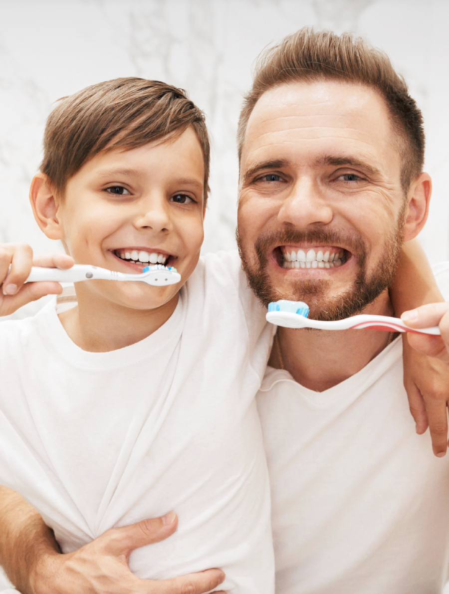 Father and son brushing teeth and showing off straight, white teeth.