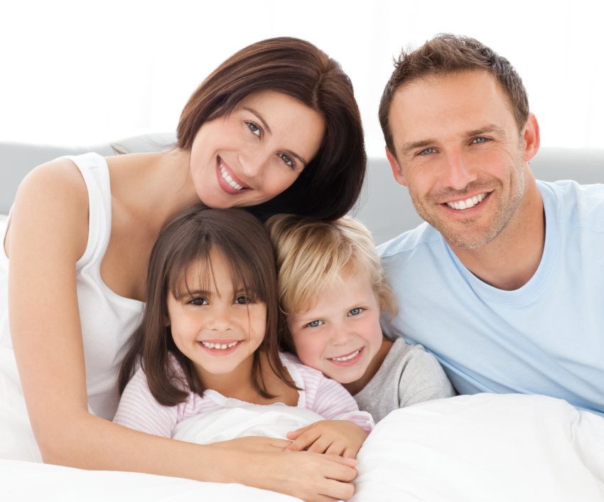 Family of four posing together happy and smiling showing perfectly straight, white teeth.