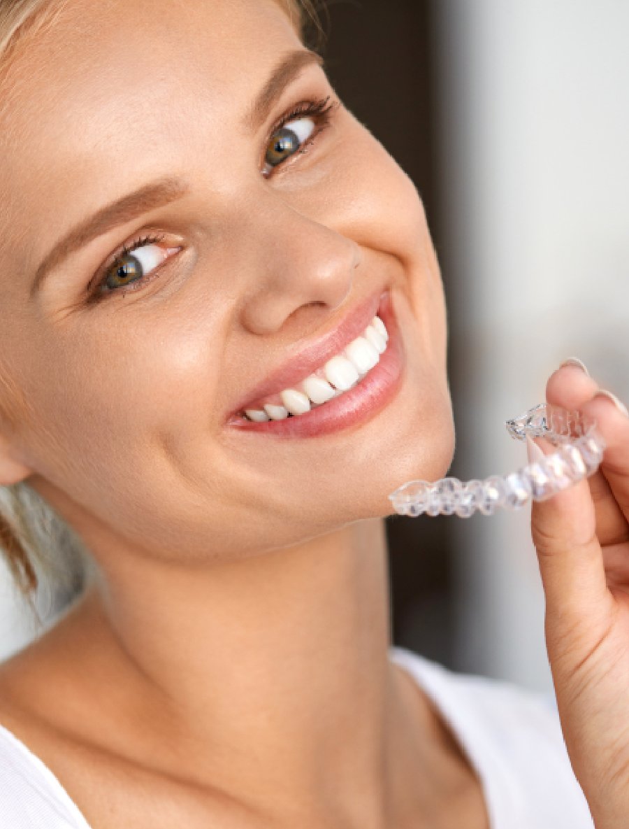 Beautiful woman smiling showing off straight, white teeth and holding Invisalign aligners in her hand.