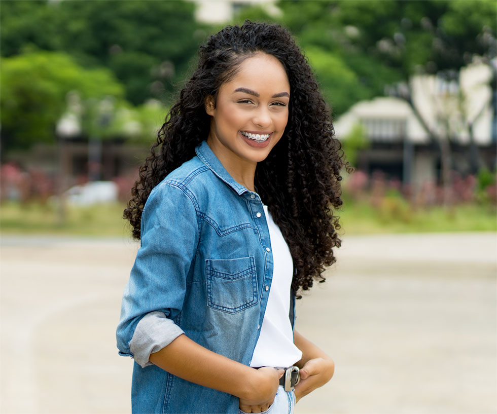 Beautiful black woman poses with hands in front pockets showing a bright, straight smile.